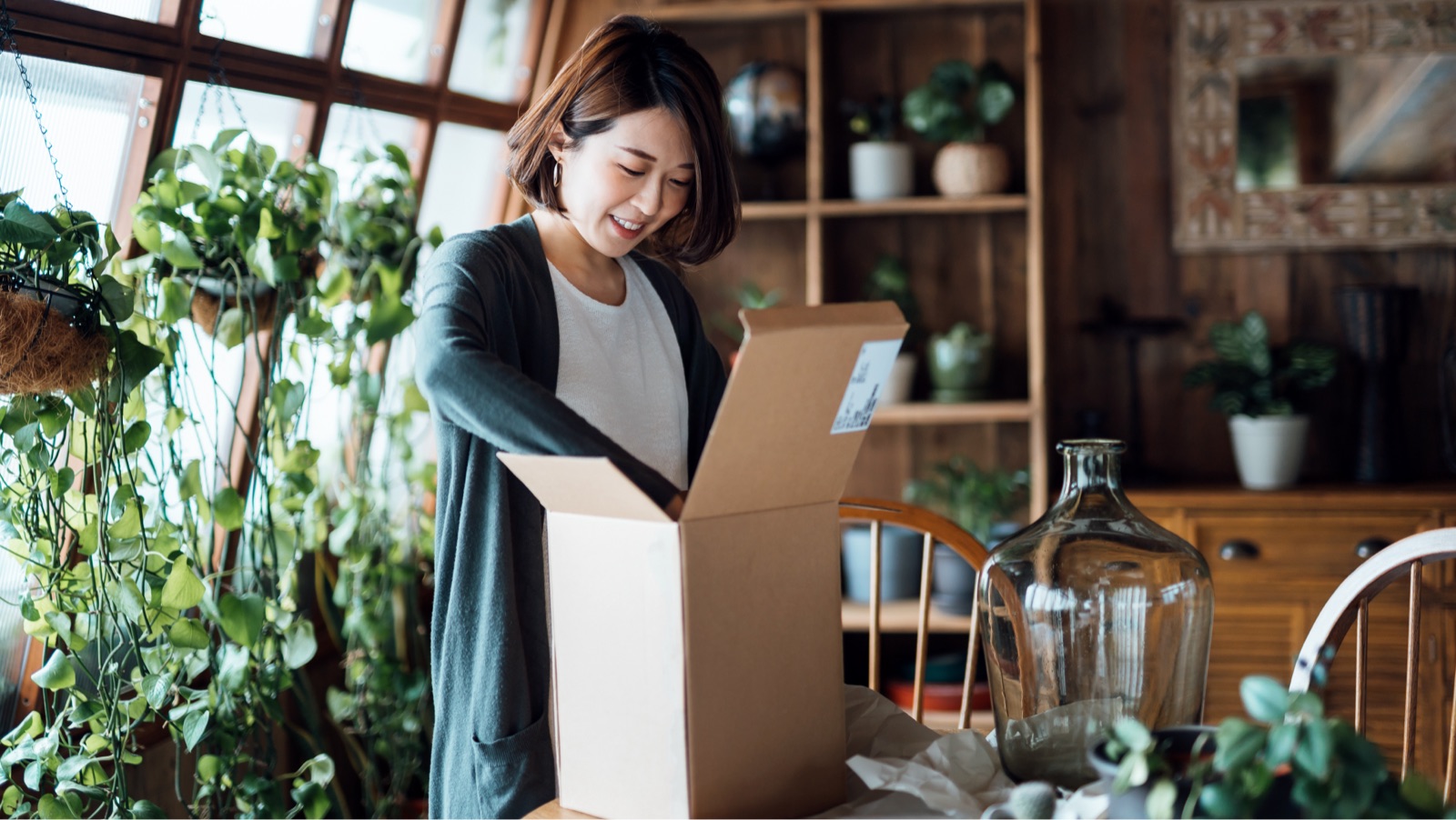Woman packing a shipping box with plants around her.