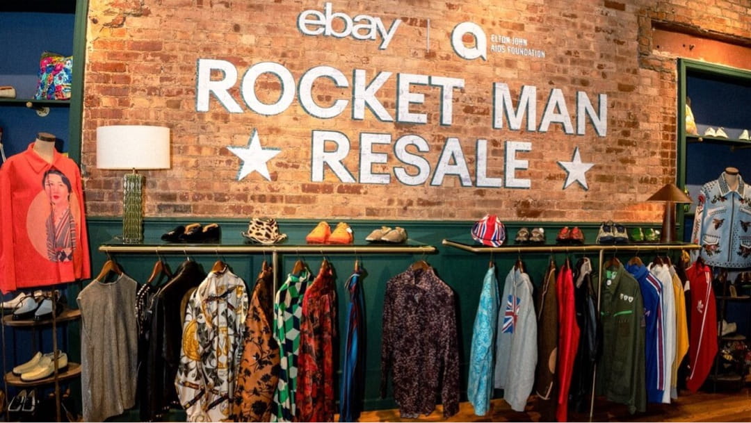 Elton John’s shirts displayed for sale under a brick wall painted with the words “Rocket Man Resale.”