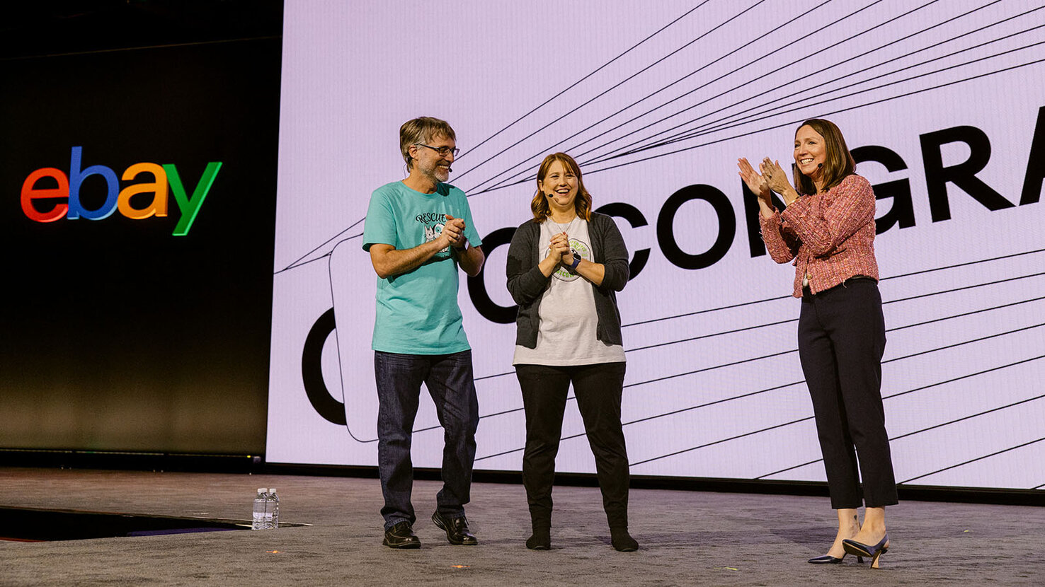 Three speakers stand onstage at eBay Open, applauding during a presentation.